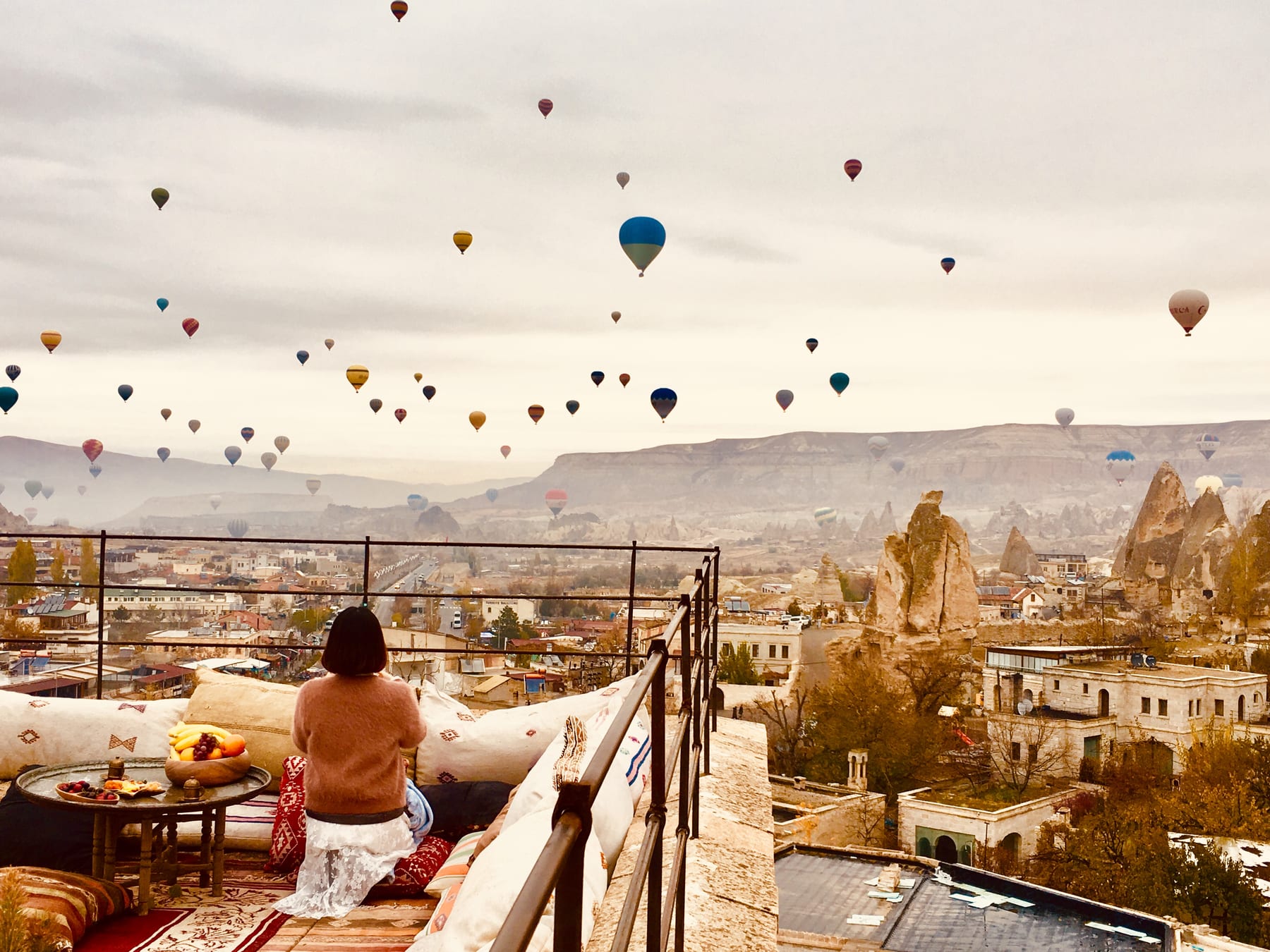 Dozens of hot-air balloons drifting over the fairy chimneys of Cappadocia at dawn, seen from a terrace