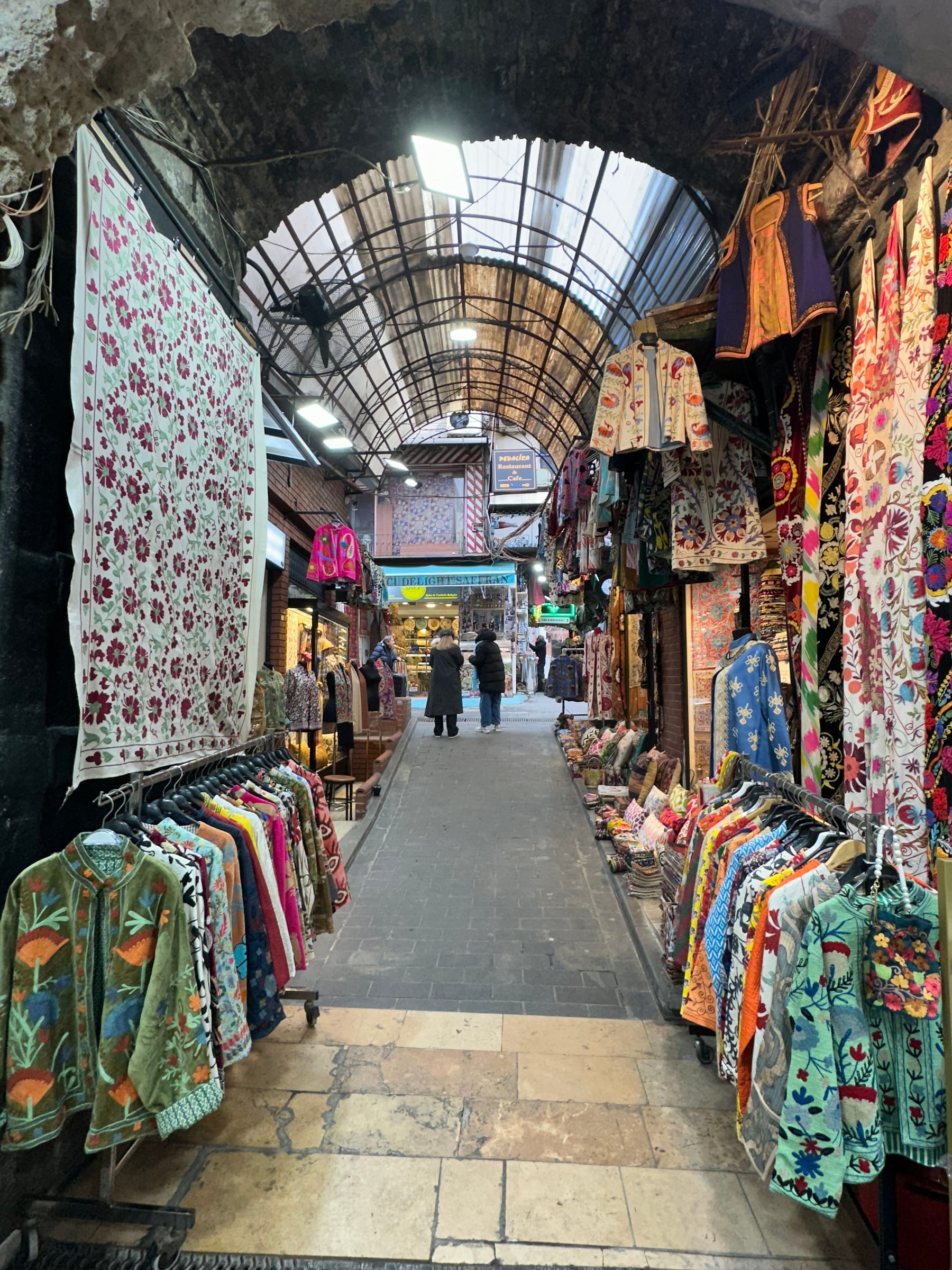 Embroidered textiles and vintage coats hanging along a vaulted lane of the Grand Bazaar bedesten in Istanbul