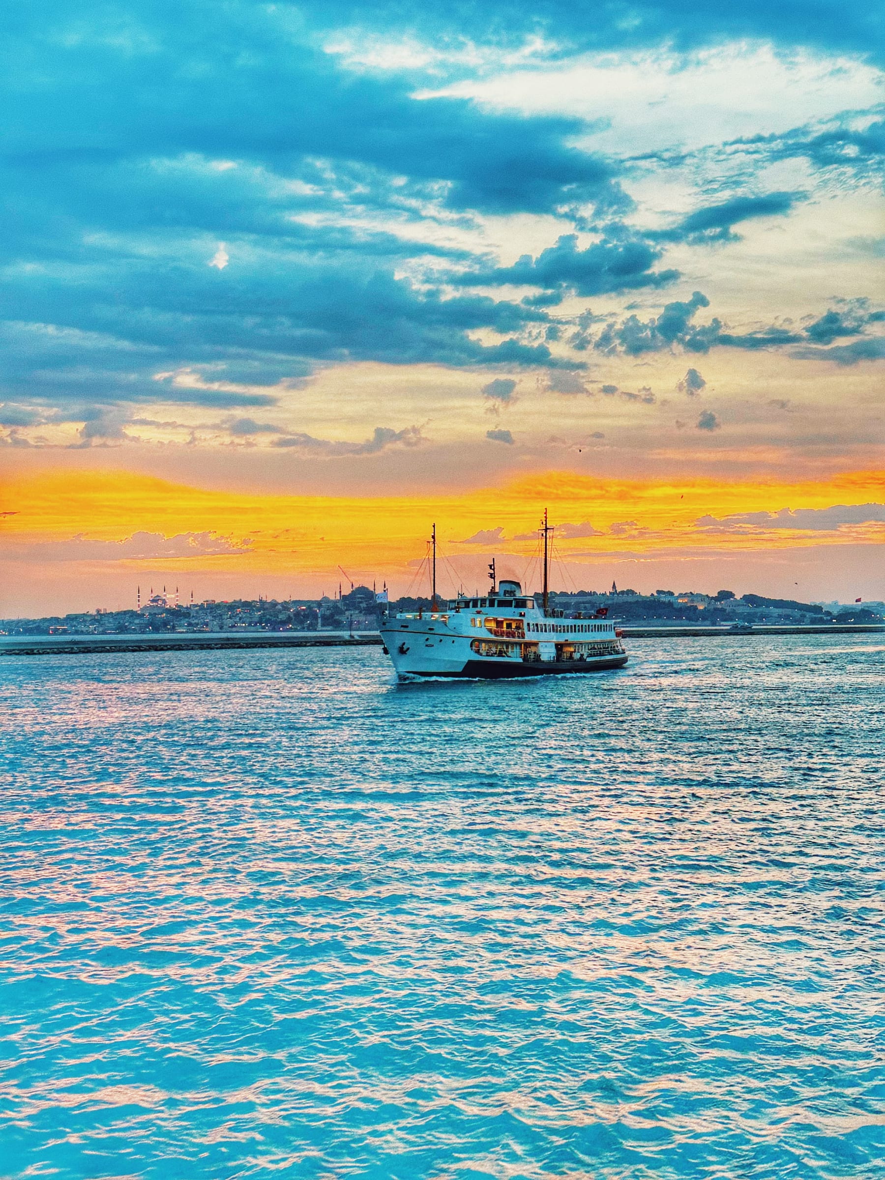 An Istanbul ferry crossing the Bosphorus at sunset, with the domes and minarets of the Old City skyline glowing on the horizon