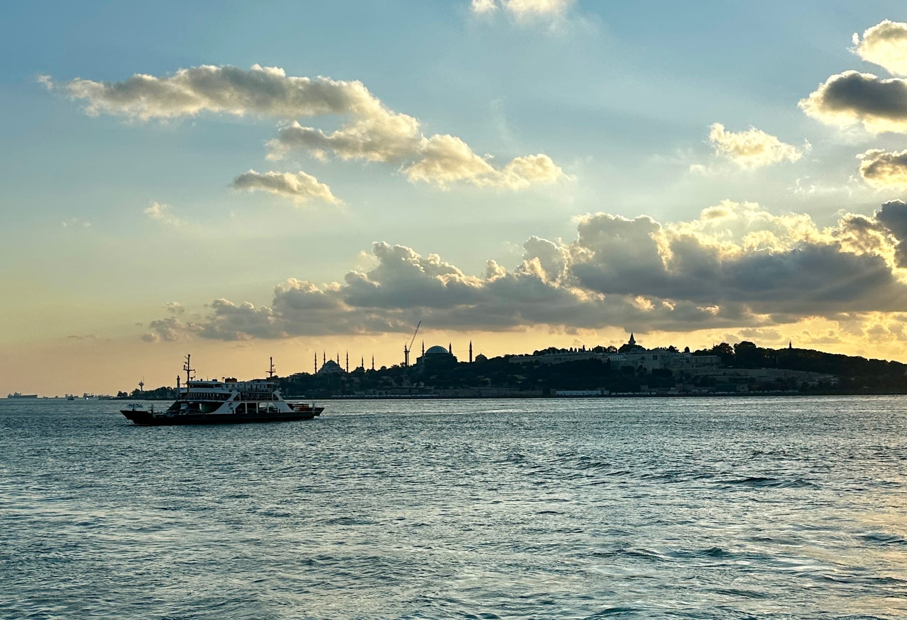 An Istanbul ferry crossing the Bosphorus at sunset, with the domes and minarets of the Old City skyline — the Blue Mosque, Hagia Sophia and Topkapi Palace — on the headland behind