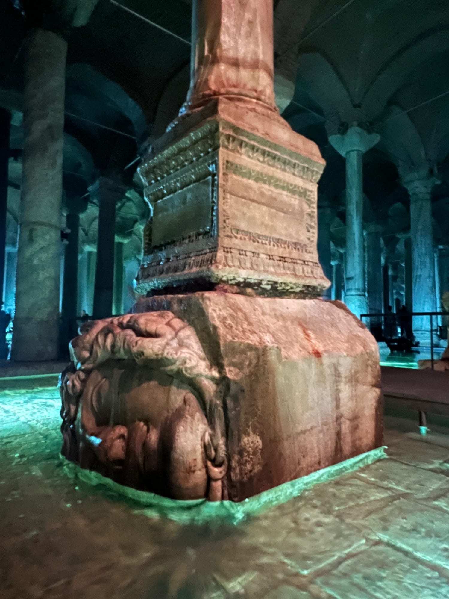 The famous upside-down Medusa head column base in the Basilica Cistern, lit in green beneath the columns of the ancient underground reservoir in Istanbul